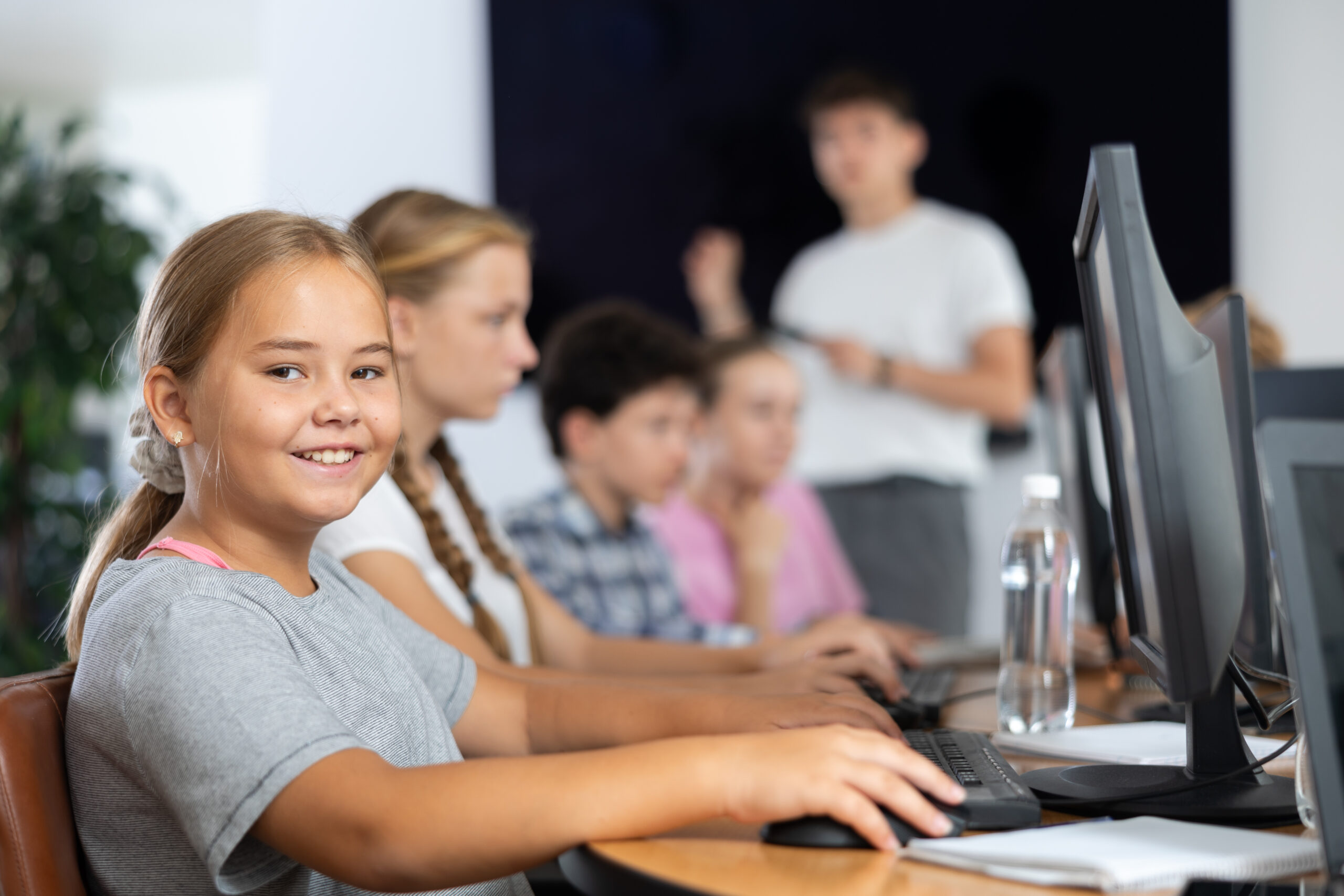 Smiling preteen girl sitting at computer table in training room